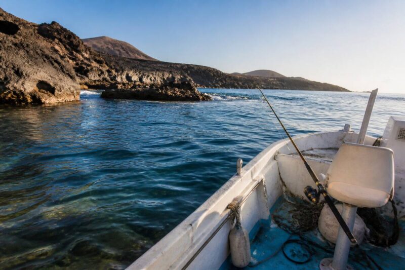 Een realistische foto van een boot om te vissen voor de rotsachtige kust van Lanzarote met heldere zee en een hengel aan boord
